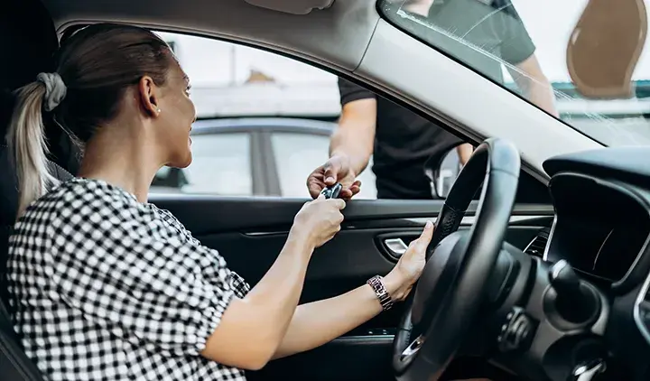 Käytettyä autoa myyvä nainen ojentaa auton kuskin paikalta avaimet miehelle